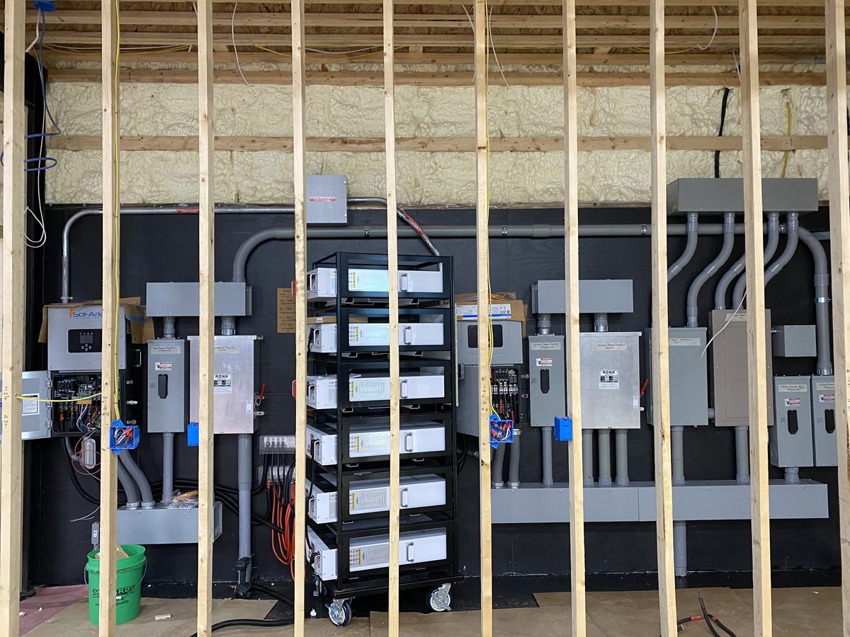 Inverter, battery rack, transfer switches and subpanels on a wall