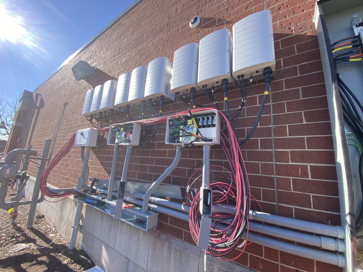 Row of SolarEdge string inverters and combiner boxes on a brick wall