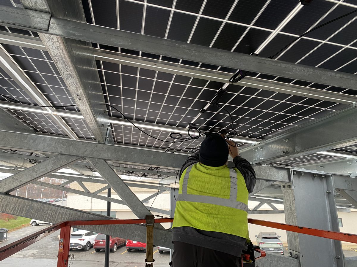 Installer wiring optimizers under a solar carport from a lift