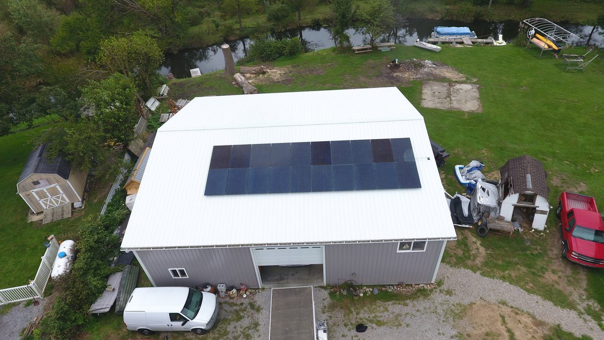 Aerial view of a solar array on a white metal pole barn roof beside a river